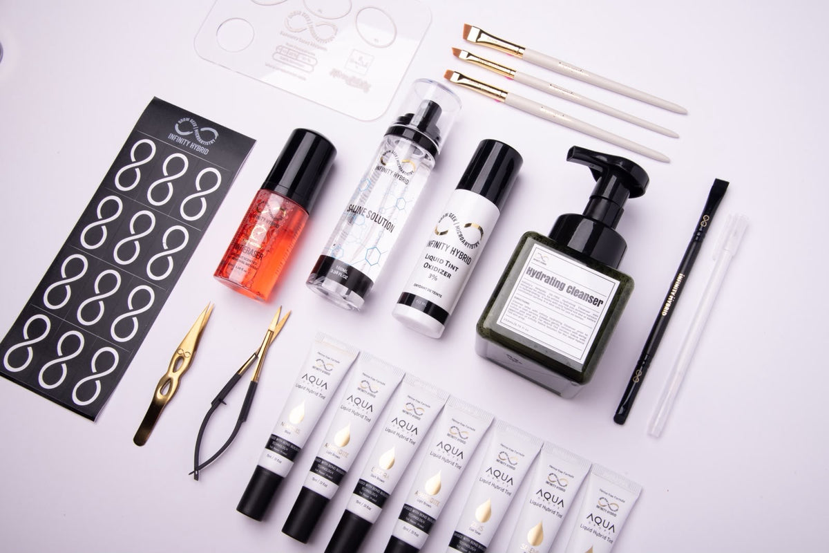 Infinity x The Brow Geek Hero Bundle, angled flat lay of Aqua Drops® hybrid brow dye boxes, liquids, brow brushes and mapping tools