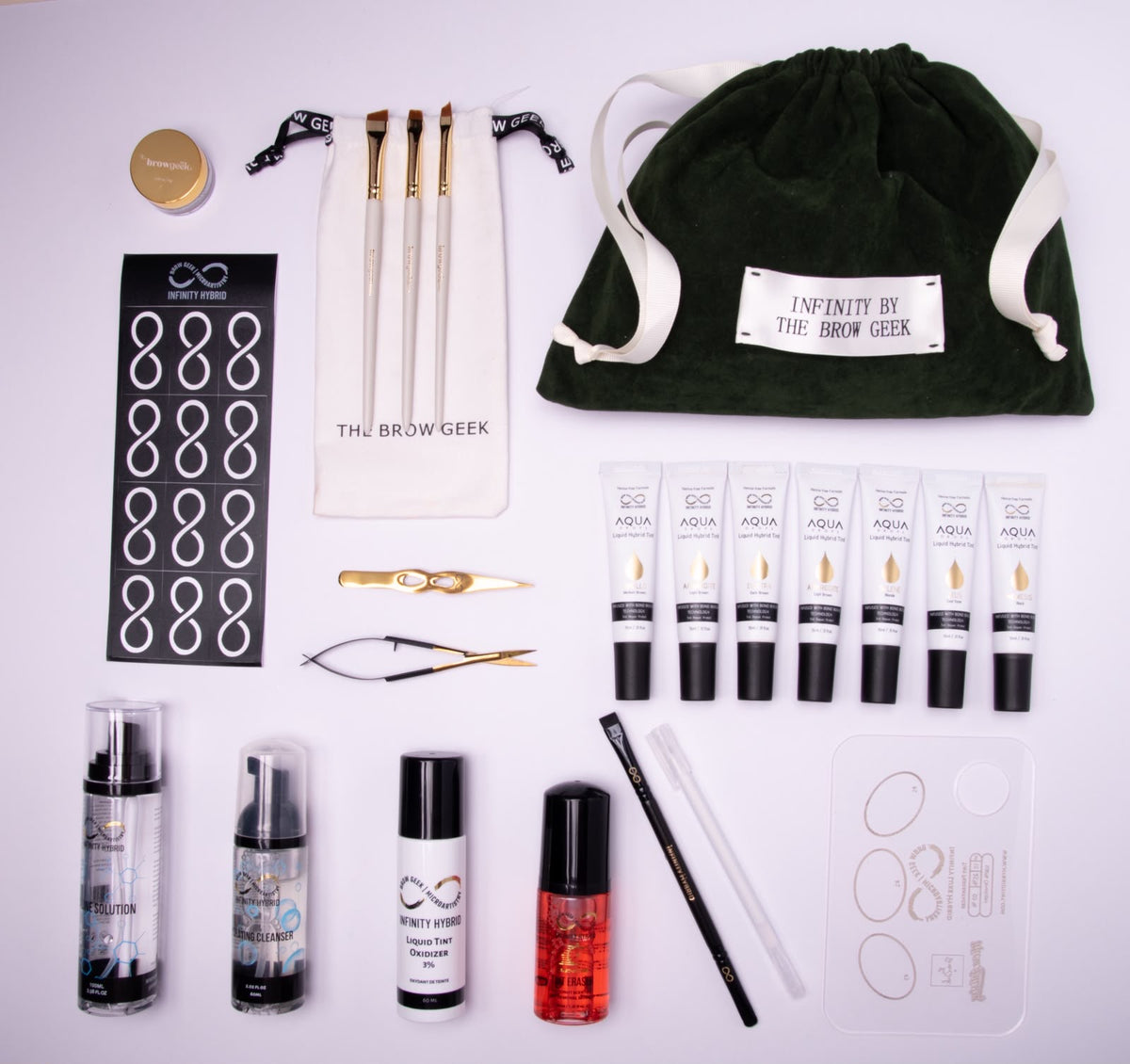 Infinity x The Brow Geek Hero Bundle flat lay: 7 Aqua Drops® hybrid brow dye shades, developer, brow cleanser, saline, Shake & Glow brow oil, brushes, tools and velvet bag